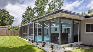 Ein modernes Haus mit einer verglasten Terrasse, einem Schwimmbad und einem gepflegten Rasen.