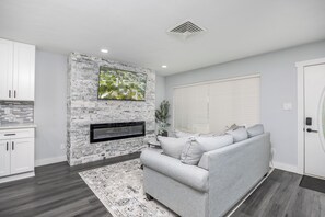 Un salon moderne avec une cheminée en pierre, un téléviseur à écran plat, un canapé gris et un tapis à motifs.
