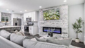 Eine moderne Küche mit weißen Schränken, Edelstahlgeräten und einem großen Fernseher, der an einer Steinwand angebracht ist.