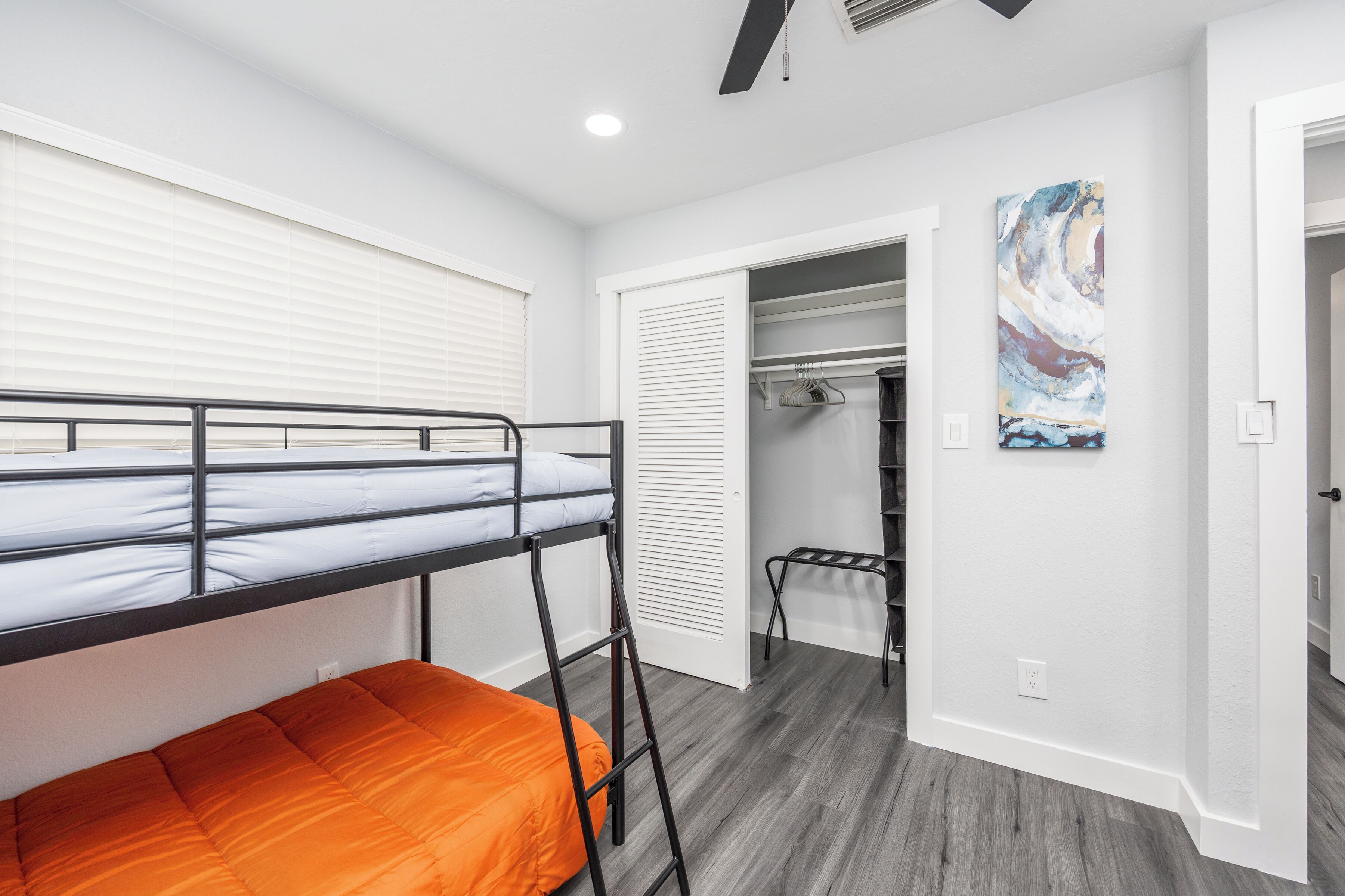 A bunk bed with an orange mattress, a walk-in closet with a hanging rod, and a painting on the wall.