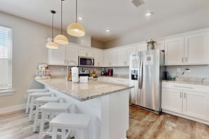 A modern kitchen with white cabinets, a granite countertop, stainless steel appliances, and pendant lighting. - Gorgeous beach house with private pool, outdoor TV & custom grill area (Orange Beach)