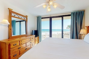 A hotel room with a large bed, a wooden dresser, a ceiling fan, a television, and a balcony with a view of the beach. - Fantastic beachside condo with pool, sauna, WiFi & central AC (Orange Beach)