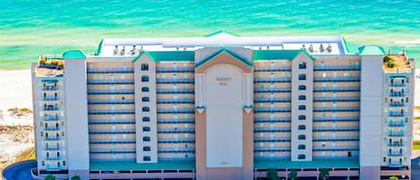 A multi-story hotel with balconies, a central entrance, and a view of the ocean.