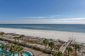 A beach view from a resort with a pool area, palm trees, and a boardwalk. - Gulf-front retreat with great view, balcony, pools, lazy river, & hot tubs (Orange Beach)
