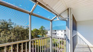 Un balcon fermé offrant une vue sur un quartier résidentiel, notamment sur un immeuble blanc doté d’un balcon.
