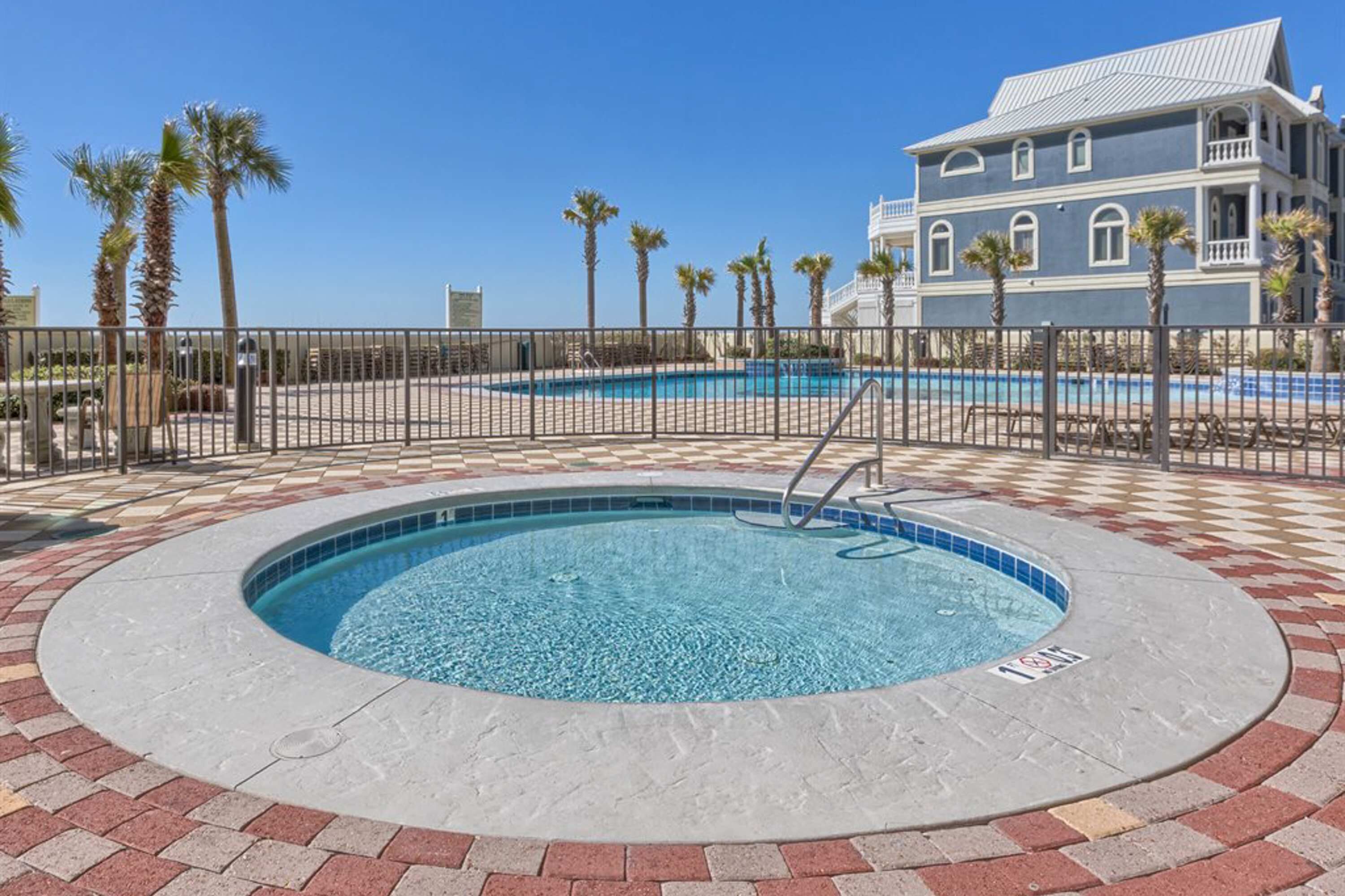 A pool area with a circular hot tub, palm trees, and a building with a blue facade.
