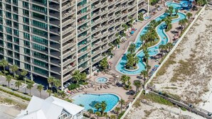 Ein Hochhaus-Hotel mit zahlreichen Balkonen, einem zentral gelegenen Poolbereich mit mehreren Pools und einer Strandpromenade.