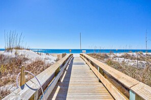 A wooden boardwalk leading to a beach with clear blue water. - Beachfront condo with Gulf views, balcony, pools, hot tubs & sports courts (Orange Beach)