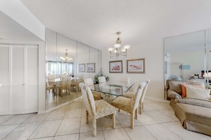 A dining area with a glass table, woven chairs, and a chandelier. - Gulf-front condo with beach view, deck, AC, pools, hot tub & tennis (Orange Beach)