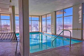 An indoor swimming pool with clear windows, a bench, and a pool ladder. - Gulf-front corner condo with wraparound balcony, pools, beach access (Orange Beach)