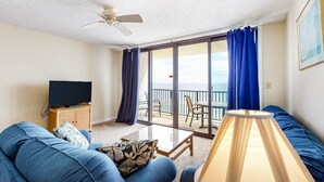 Uma sala de estar com sofá, televisão, luminária e varanda com vista.