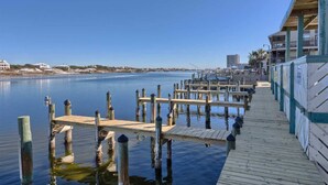Um cais à beira-mar com estacas de madeira e um deck de madeira que leva a um edifício com varandas.
