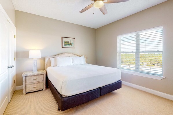 A bedroom with a bed, a nightstand, a ceiling fan, a window with blinds, and a framed picture on the wall.