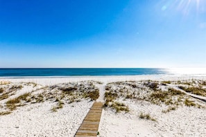 Ein Strandweg führt zum Meer, vorbei an Dünen, unter einem klaren Himmel.