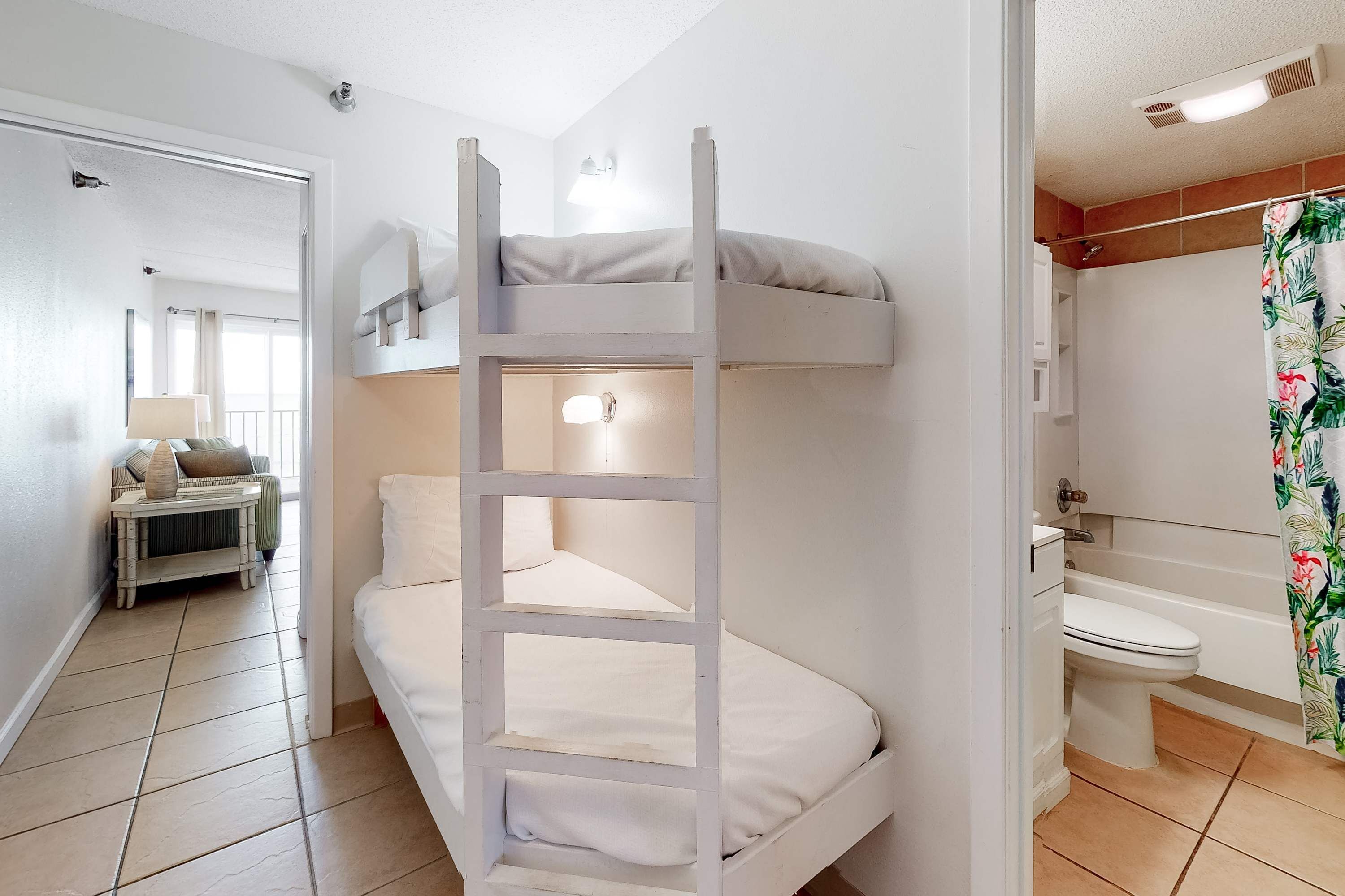 A bunk bed with a ladder, a bathroom with a toilet and shower, and a hallway with a lamp.