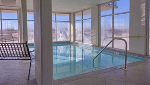 Une piscine intérieure avec des parois en verre transparent, un escalier métallique et un banc.