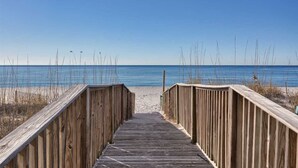 Une promenade en bois qui mène à une plage, avec un ciel dégagé.