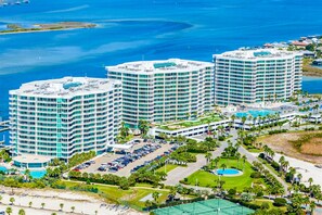 A high-rise hotel with multiple balconies, a parking lot, and a pool area. - Gulf-front 8th-floor Condo with balcony, pool, hot tubs, & tennis courts (Orange Beach)