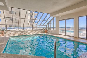An indoor swimming pool with clear blue water, large windows, and a view of the beach. - 6th-Floor Oceanfront Condo w/Balcony, AC, Shared Pools, Sauna, Free WiFI, Gym (Orange Beach)