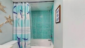 Une salle de bain avec une baignoire, des toilettes et un rideau de douche orné de motifs d’étoiles de mer.