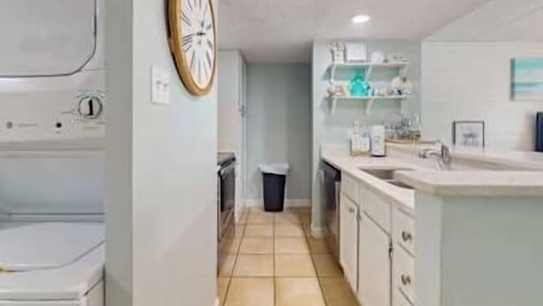 Une petite cuisine équipée d’un évier, de placards et d’une horloge murale.