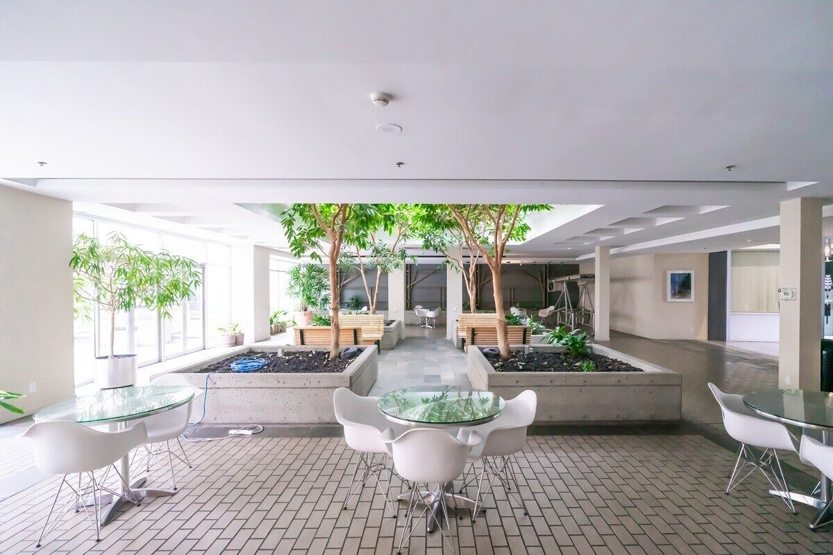 Un espacio interior moderno con un jardín central, rodeado de arreglos de asientos y una mesa de vidrio.