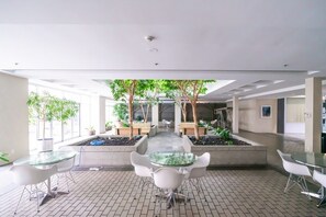 Ein moderner Innenraum mit einem zentralen Gartenbereich, umgeben von Sitzgelegenheiten und einem Glastisch.
