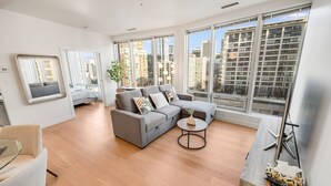 A modern living room with a grey sofa, a round coffee table, and a view of tall buildings through large windows. - Modern & Cozy Stay in Prime DT (Vancouver)