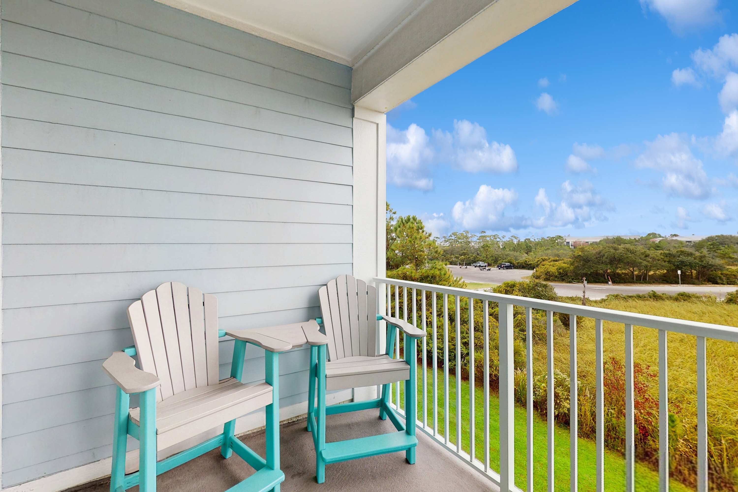 A porch with two Adirondack chairs and a white railing overlooking a green landscape.