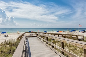 A wooden boardwalk leading to a beach with umbrellas and a flag. - Beachfront corner condo with stunning Gulf views, pools, hot tub & fitness center (Orange Beach)