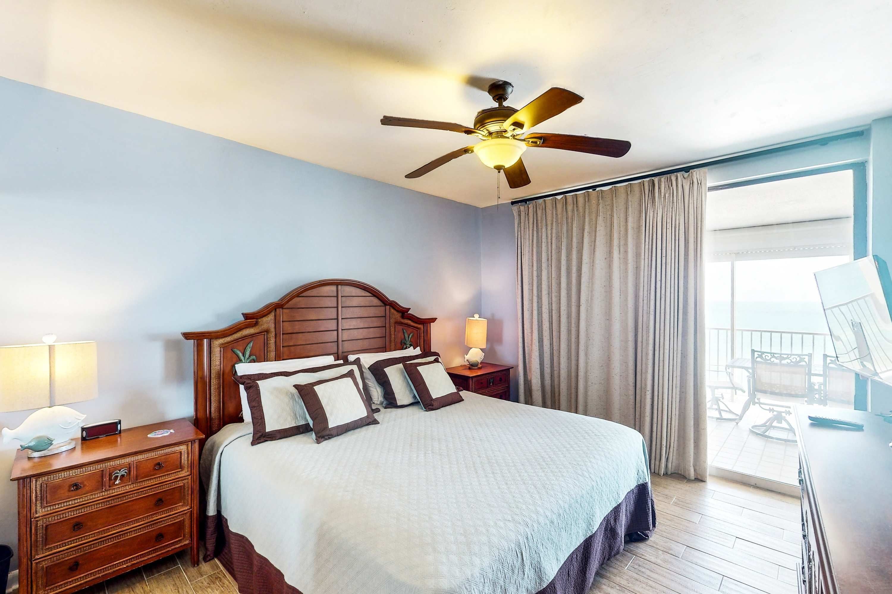 A hotel room with a bed, wooden headboard, bedside table with lamp, and a view of the balcony.