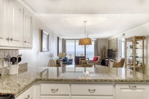 A kitchen with granite countertops, white cabinets, a hanging light fixture, and a view of the outdoors. - Fourth-floor beach condo w amazing views, indoor pool, & beach access (Orange Beach)