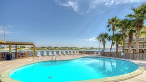 Ein Swimmingpool mit Holzterrasse, Palmen und Blick auf das Wasser.