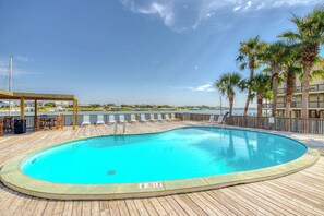 A swimming pool with a wooden deck, palm trees, and a view of the water. - Fourth-floor beach condo w amazing views, indoor pool, & beach access (Orange Beach)
