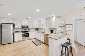 A modern kitchen with white cabinets, stainless steel appliances, a marble countertop, and a wooden floor. - Beach front paradise w/ beautiful views, outdoor pool, & sauna (Orange Beach)