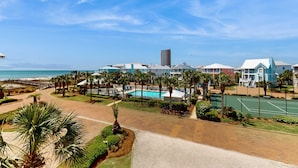 Een resort met een zwembad, tennisbaan en uitzicht op het strand.