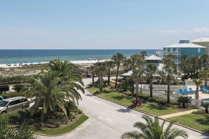 A resort with a beach view, palm trees, and a pool area. - Beach view beach home w community outdoor pool, sun deck & private beach (Orange Beach)