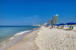 Ein Strand mit Sand, Wasser und einer Reihe blauer Sonnenschirme.