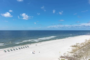 A beach with a wooden boardwalk, umbrellas, and a clear sky. - Waterfront condo w/ open layout, Gulf views, indoor & outdoor pools, & hot tub (Orange Beach)