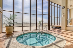 An indoor swimming pool with clear views through large windows, a clock on the wall, and a potted plant. - Waterfront condo w/ open layout, Gulf views, indoor & outdoor pools, & hot tub (Orange Beach)