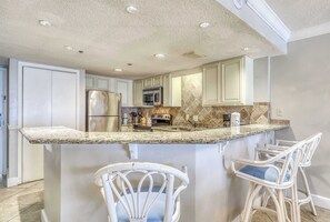 A kitchen with white cabinets, a stainless steel refrigerator, a microwave, and a granite countertop. - Waterfront condo w/ open layout, Gulf views, indoor & outdoor pools, & hot tub (Orange Beach)