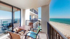 Ein Balkon mit Tisch und Stühlen, Blick auf den Strand und ein Gebäude mit Balkonen.