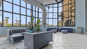 Eine geräumige Lobby mit großen Fenstern, einem blauen Sofa, einem Blumentopf und einem Fliesenboden.