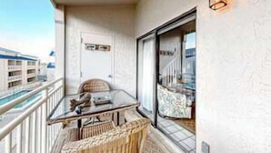 Uma varanda com mesa de vidro, cadeiras de vime, um tapete pequeno e vista para um edifício à distância, sobre a água.