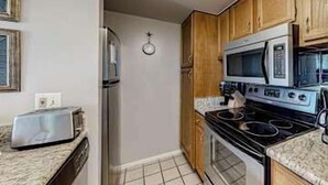 Cozinha compacta com geladeira, micro-ondas, fogão e torradeira na bancada.