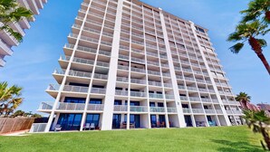 Ein mehrstöckiges Hotel mit Balkonen, einer flachen Dachterrasse und einer Grünfläche davor.