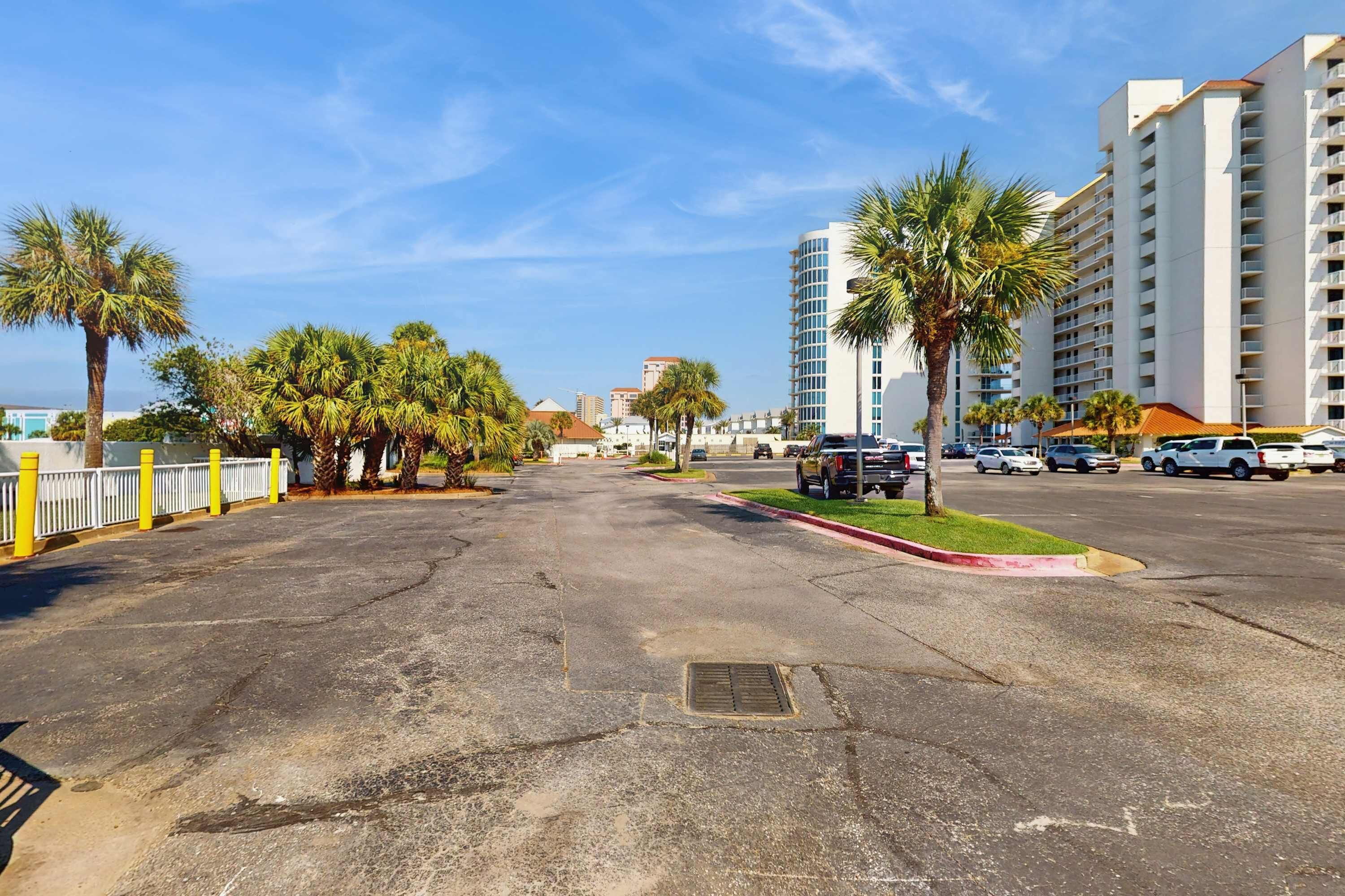 A wide street with palm trees, parked cars, and high-rise buildings.