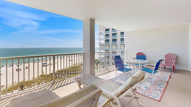 Ein Balkon mit Blick auf Strand und Meer, ein Tisch mit Stühlen und ein gemustertes Teppich.