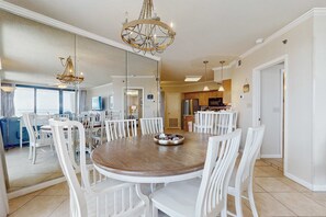 A dining area with a round table, white chairs, and a chandelier. - Gulf-front condo with furnished balcony, pools & hot tub (Orange Beach)