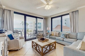 A spacious living room with a sofa, a coffee table, and a balcony with a view of the sea. - Gulf-front condo with furnished balcony, pools & hot tub (Orange Beach)